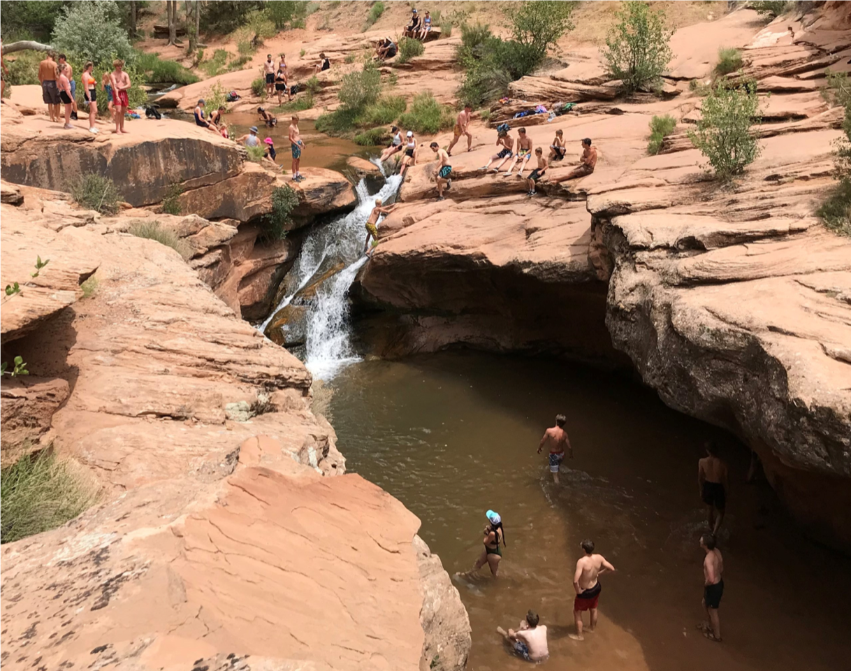 People are gathered around a waterfall and swimming hole at Mill Creek.