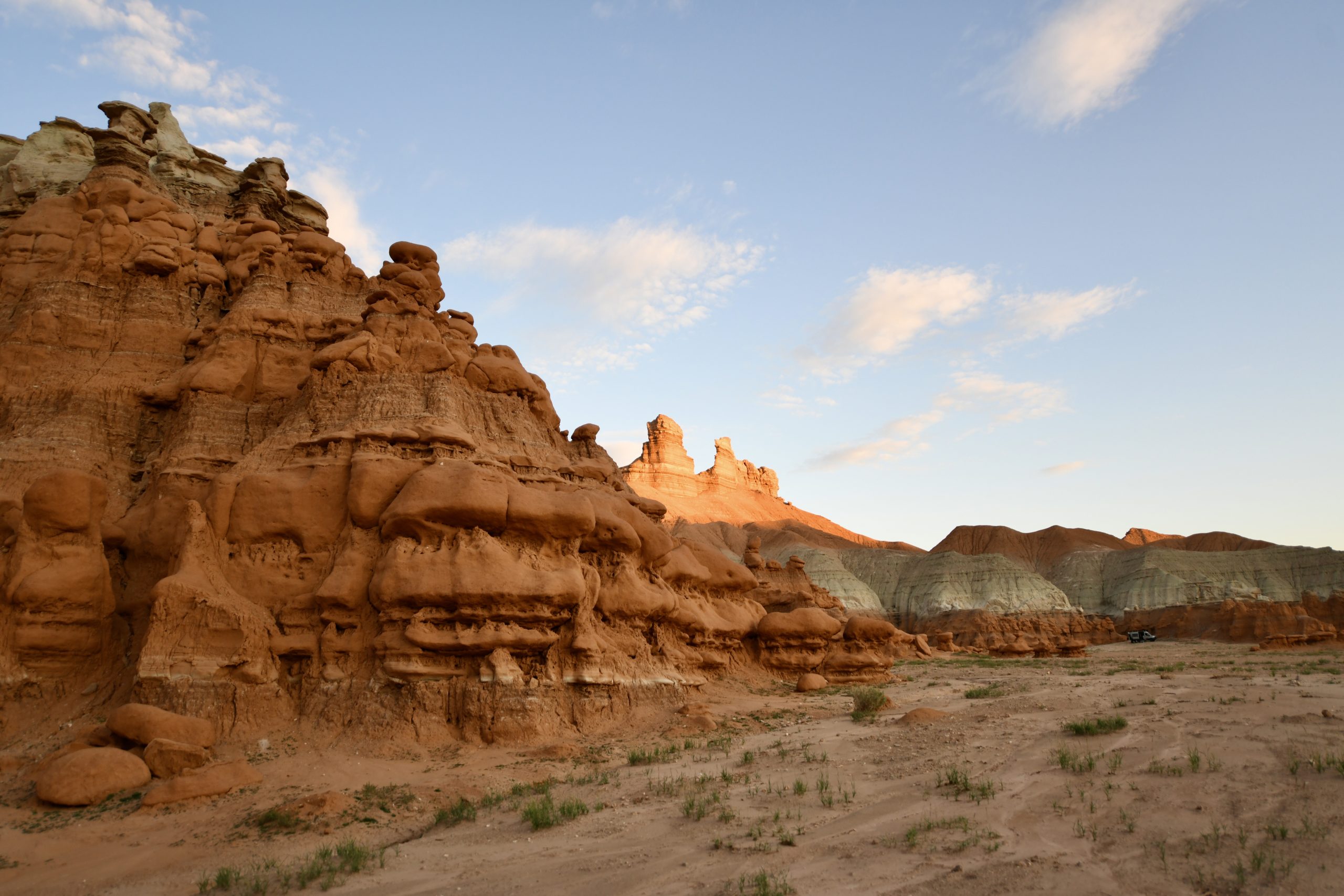 Orange hoodoo formations are in the foreground. In the background, a set of two sandstone towers is illuminated by the sun, making them glow.