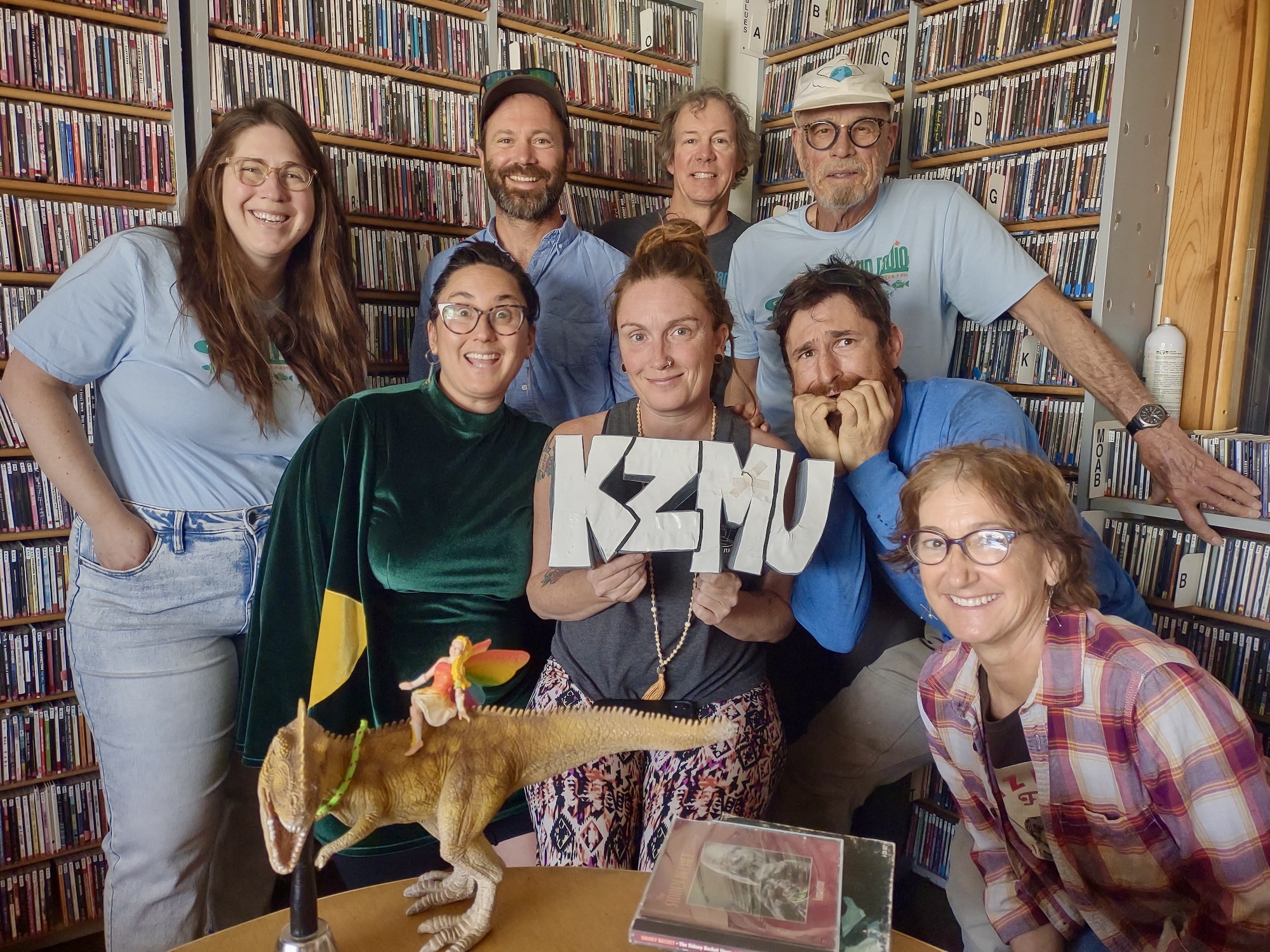 KZMU staff and volunteers posed for a celebratory photo at the station. They are holding up a sign that says "KZMU."