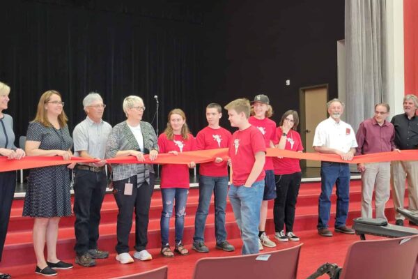 A middle school student walks up to a line of adults, most of them school district employees or local leaders, who are holding a large red ribbon.