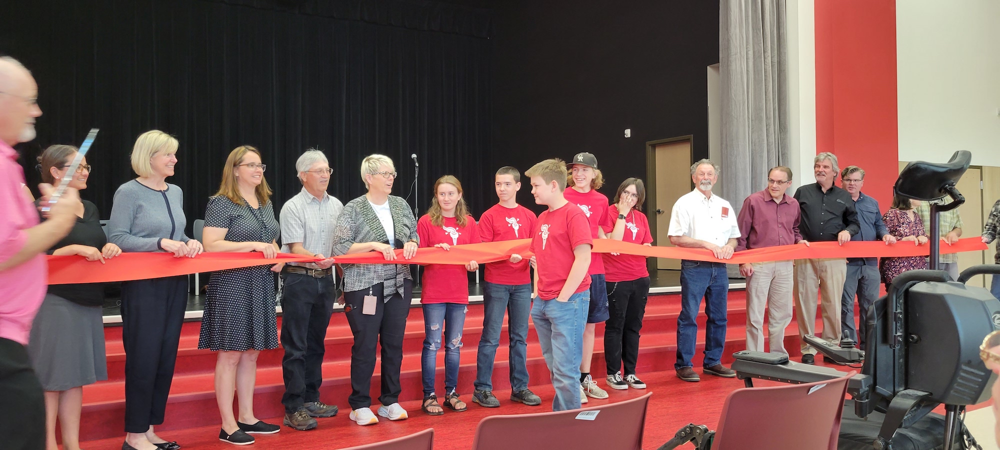 A middle school student walks up to a line of adults, most of them school district employees or local leaders, who are holding a large red ribbon.