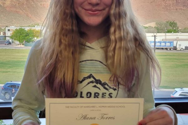Eighth-grader Alana Torres stands in front of a window with a view of the valley wall. She holds a certificate naming her as a student of the month.