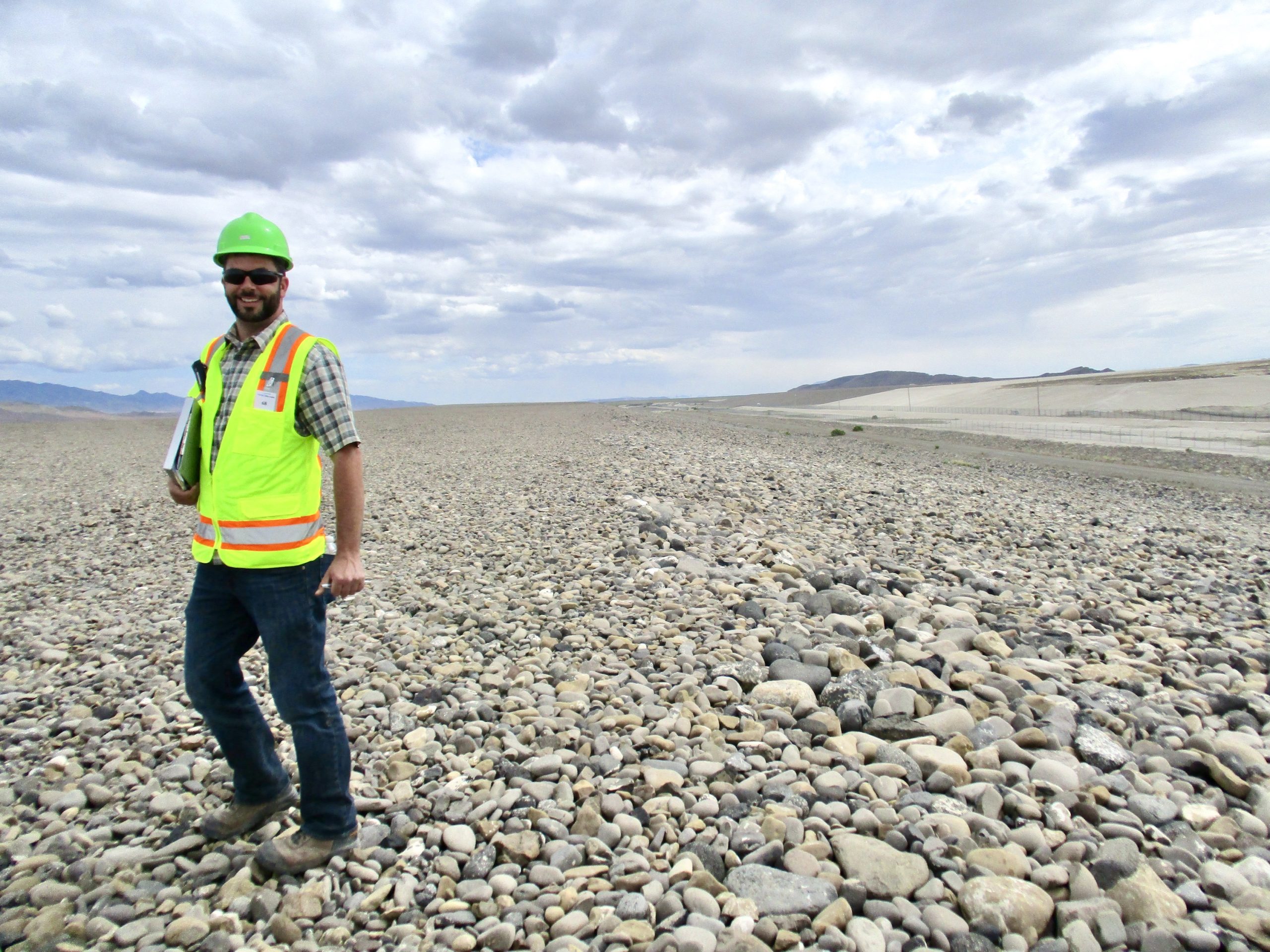 Evan Tyrrell, dressed in a hard hat and high-vis vest, stands in a field of rocks.