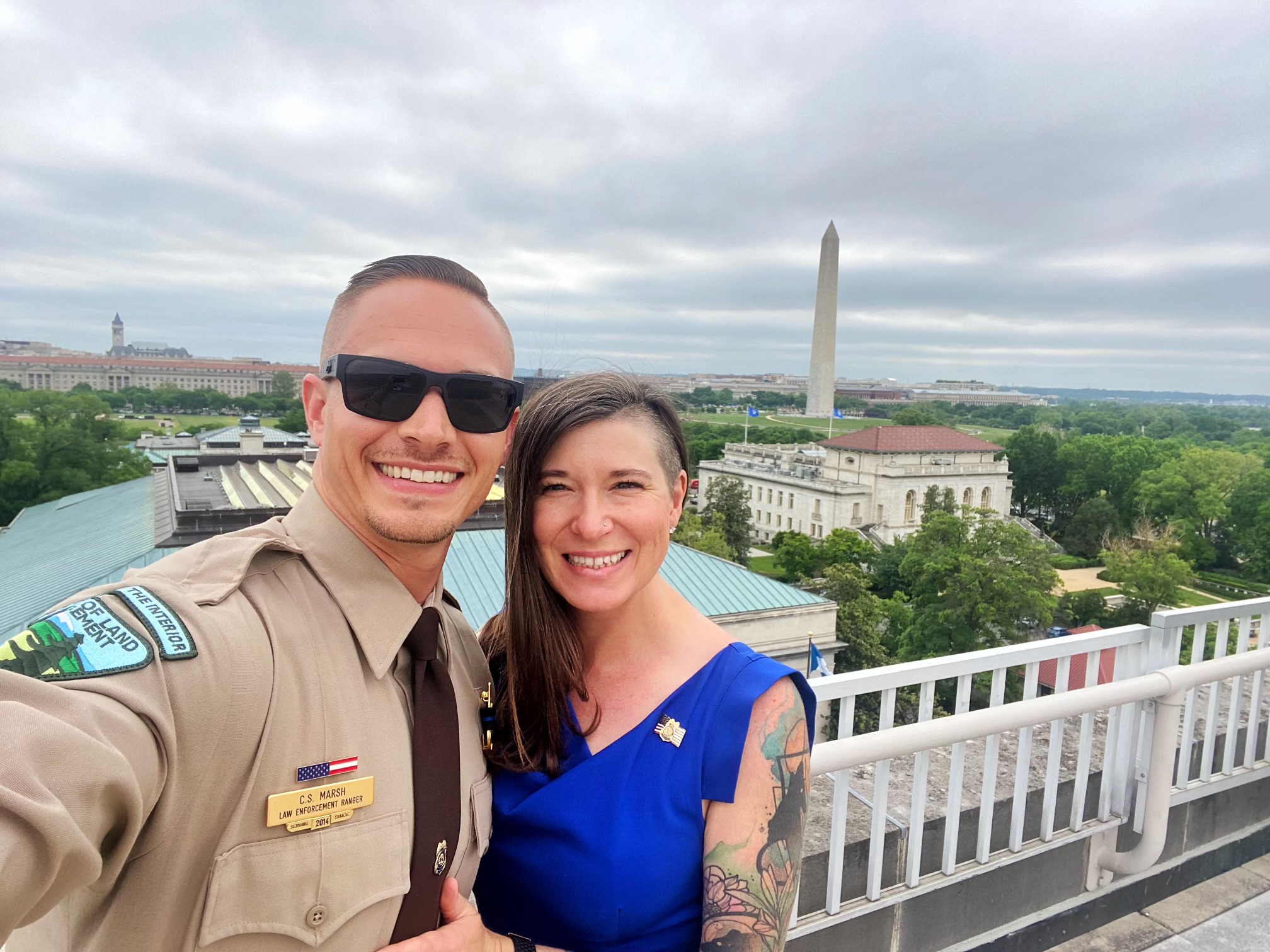 Cody Marsh and his fiancée are standing on the balcony of the Department of the Interior in Washington D.C. In the background is the Washington Monument.