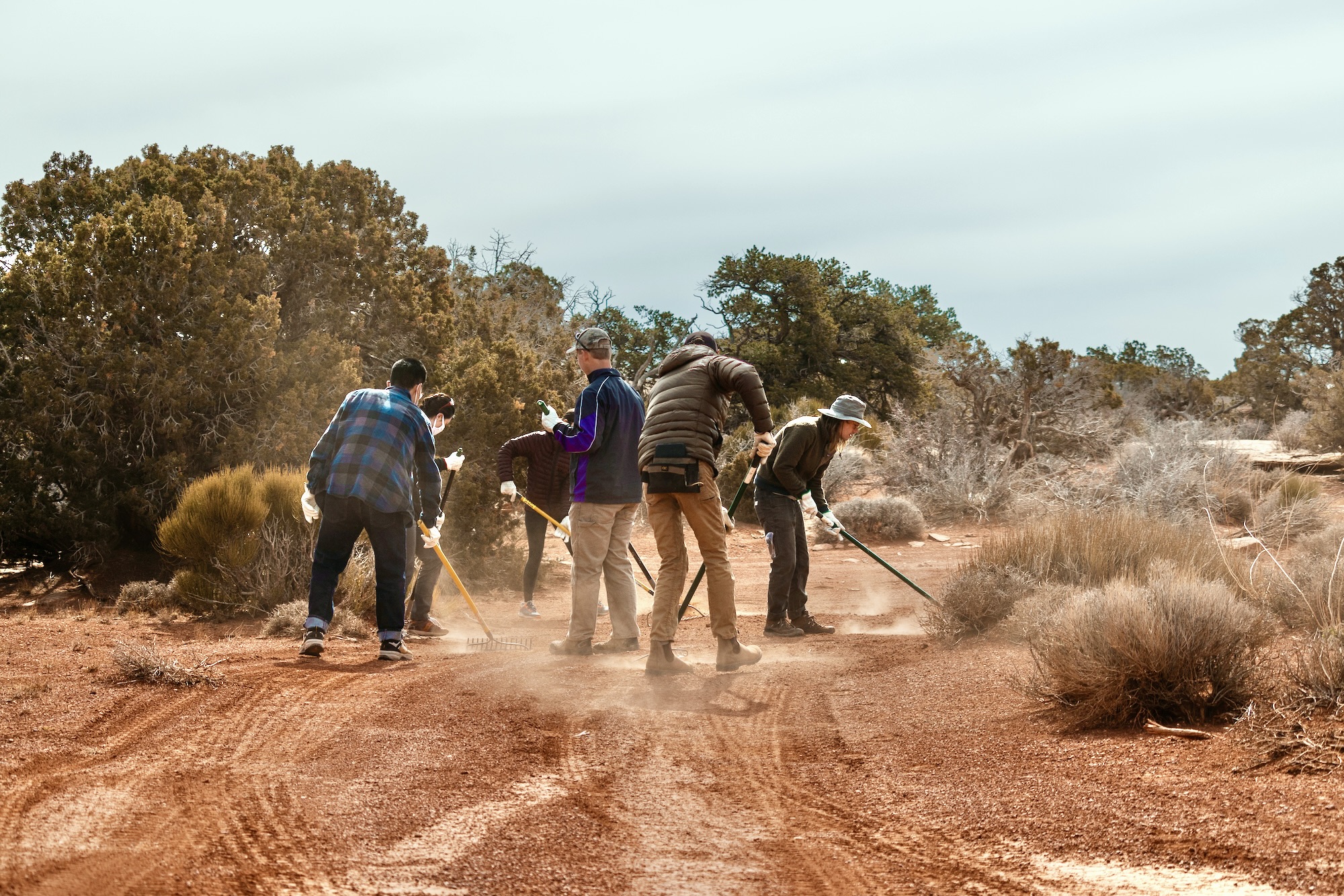 A group of people rake a trail.