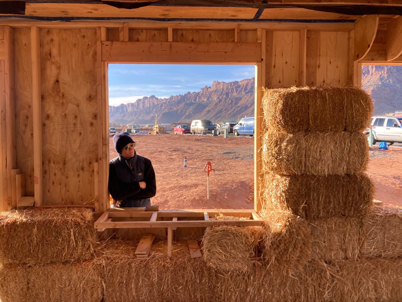A person stands in the window of an under-construction straw bale home.