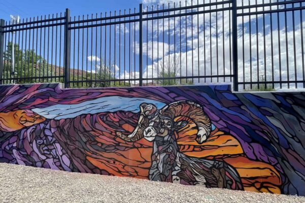 The mural was painted on a concrete wall behind the facility. It depicts a bighorn sheep in front of an arch at sunset, painted in a "stained-glass" or geometric style.
