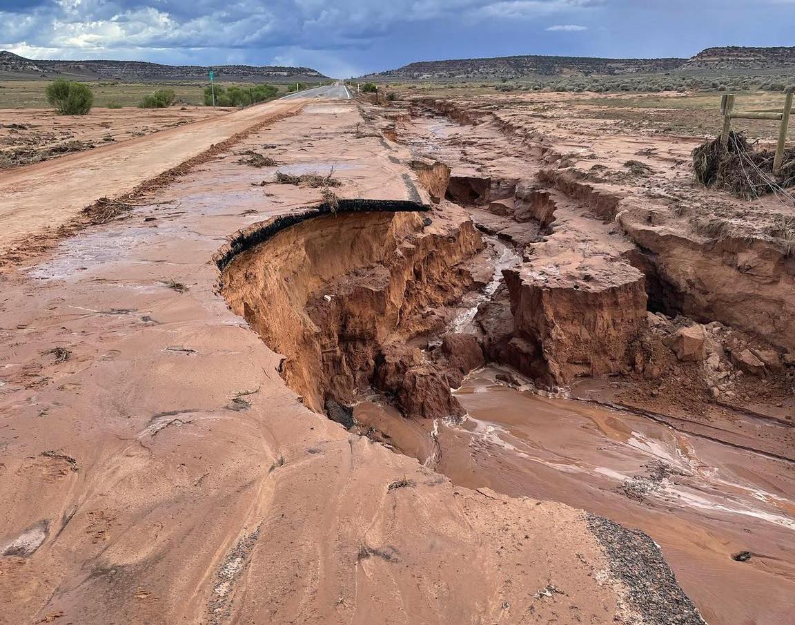 The damaged highway where State Route 211 meets Highway 191 in San Juan County: a chunk of the highway in the right lane looking north was washed out. In the background, more storm clouds loom ominously.