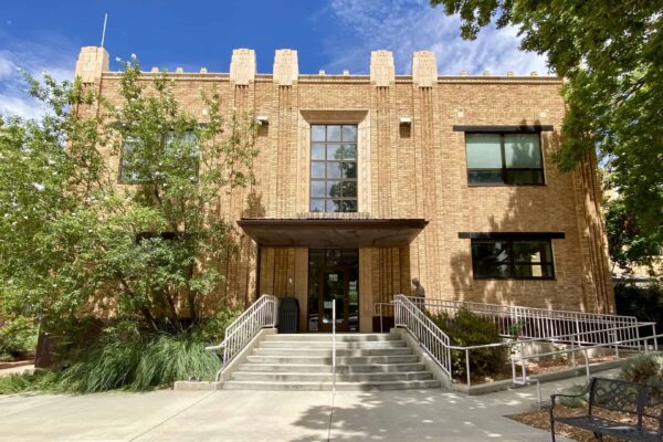 The City Hall building, pictured in the summer: it's brightly lit and surrounded by plants.