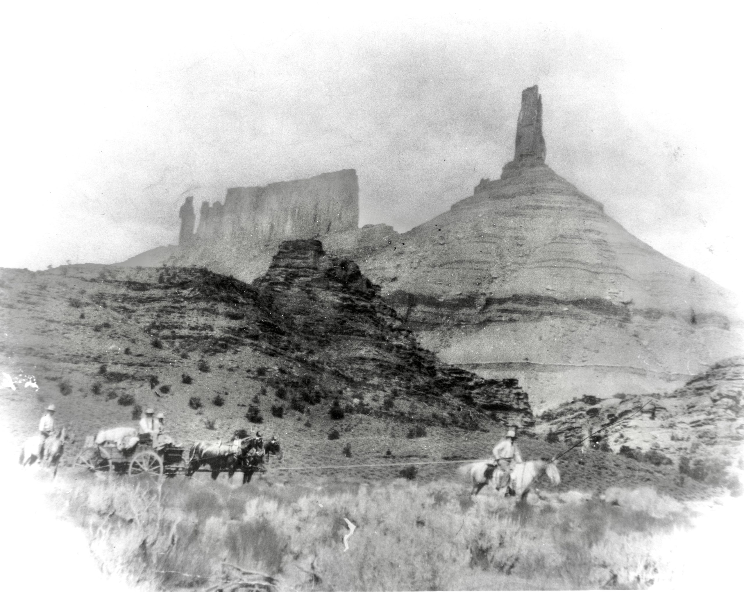 A smudged black and white photo shows four riders in front of Castle Valley; because of the lighting and picture-quality, they look almost ghost-like.