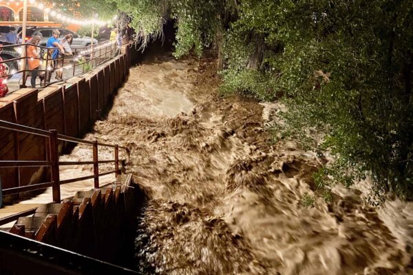 Brown and foamy floodwaters rage across the Mill Creek pathway near the Main Street bridge.