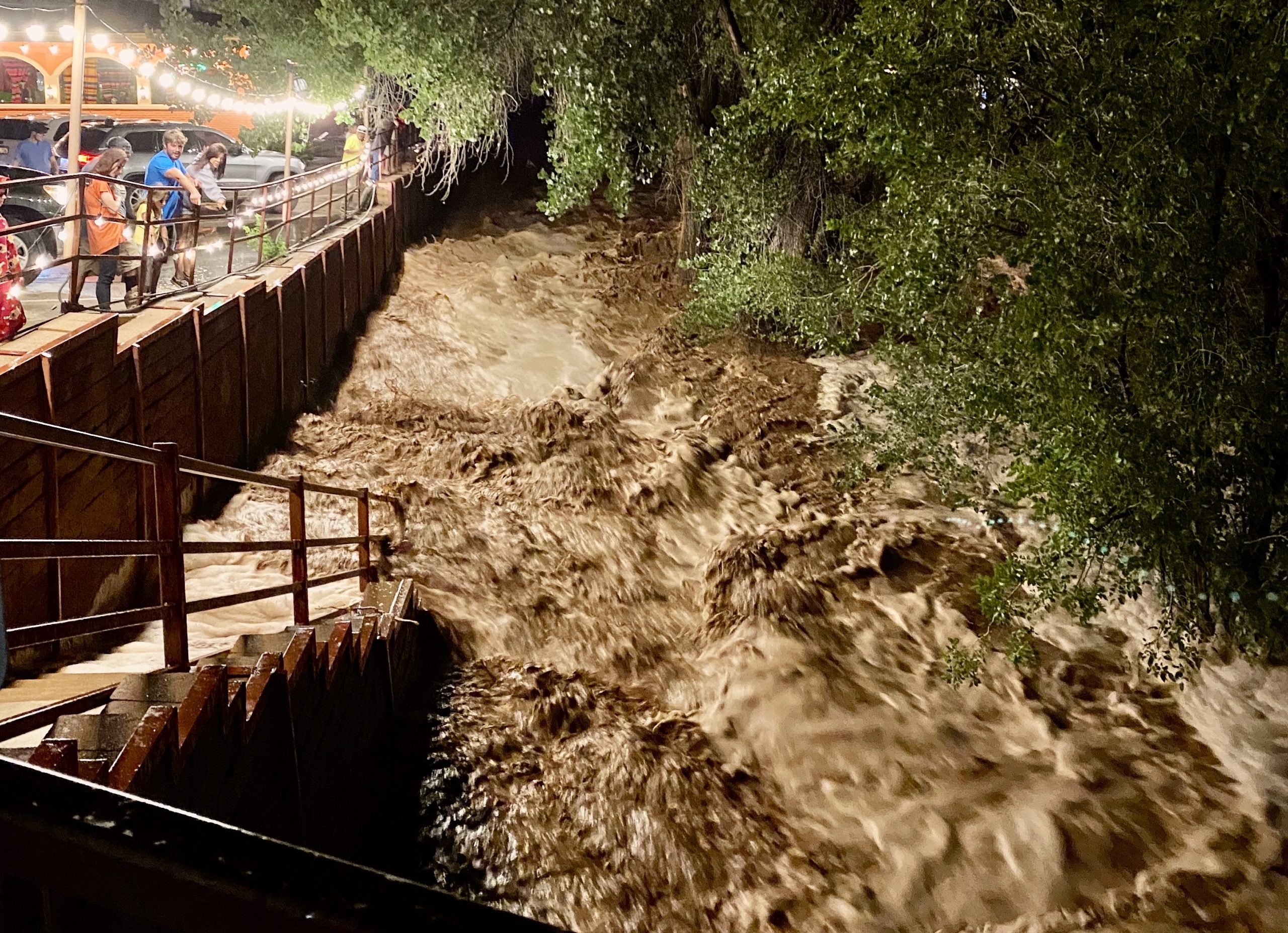 Brown and foamy floodwaters rage across the Mill Creek pathway near the Main Street bridge.