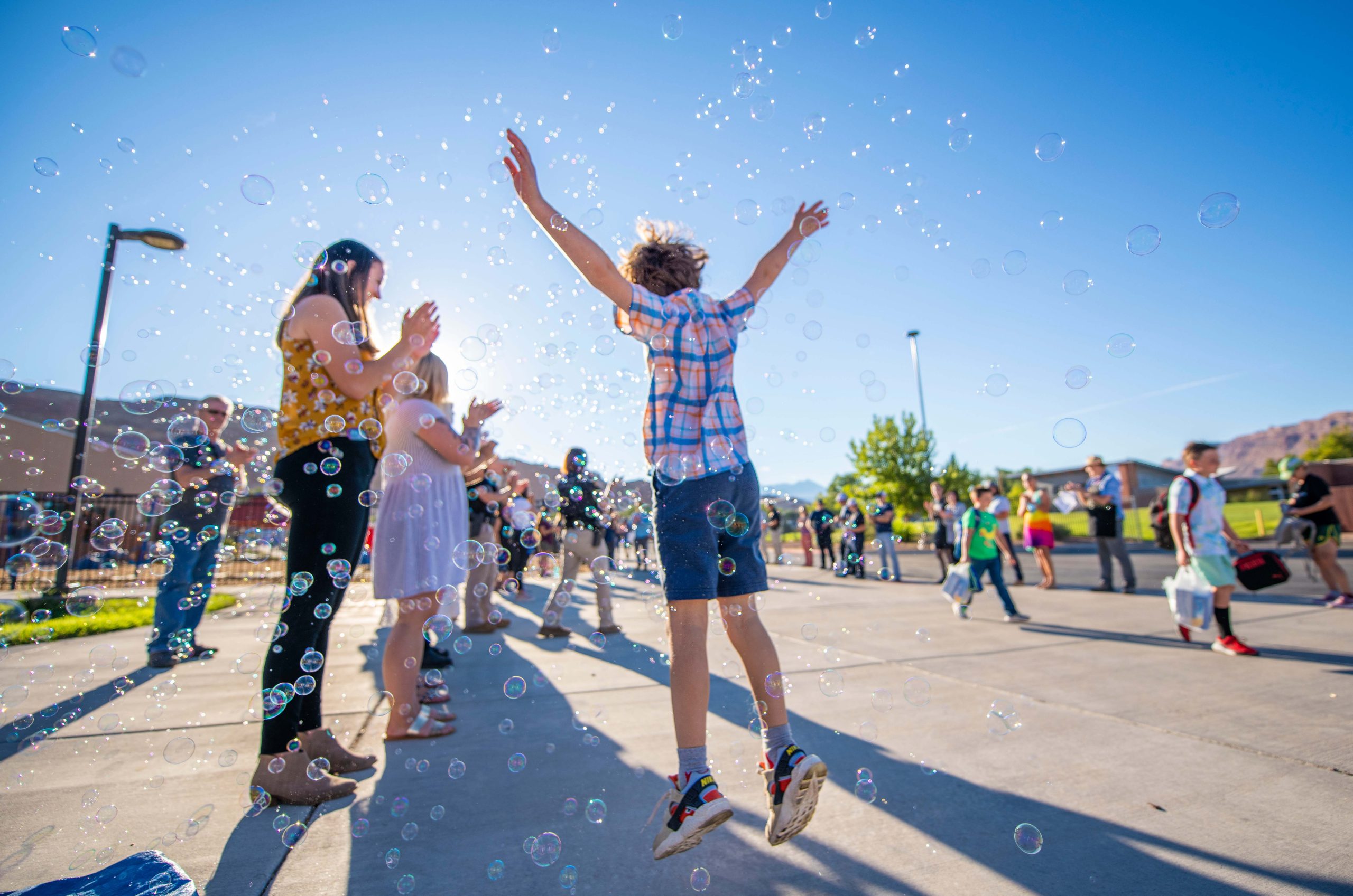 An elementary school student jumps through a cloud of bubbles on the first day of school: he is a few inches off the ground, his hands flung behind him jubilantly.