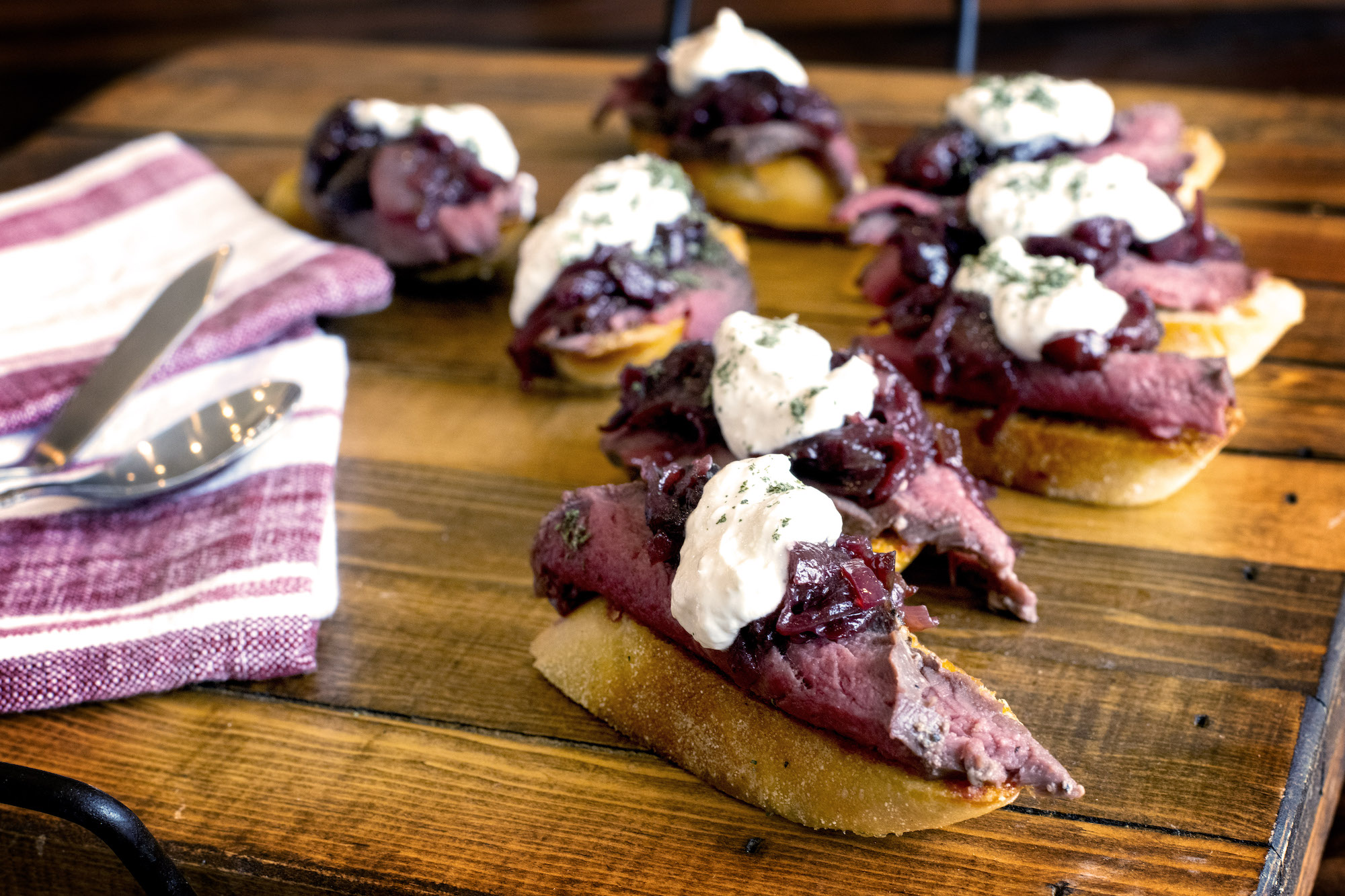 Seven pieces of toast with venison and cherry jam are artfully spread across a table. They look delicious!