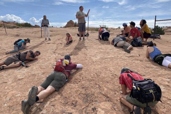 Steve Leavitt is standing in the middle of a circle of people who are all laid out on the ground, observing lichen on slickrock.