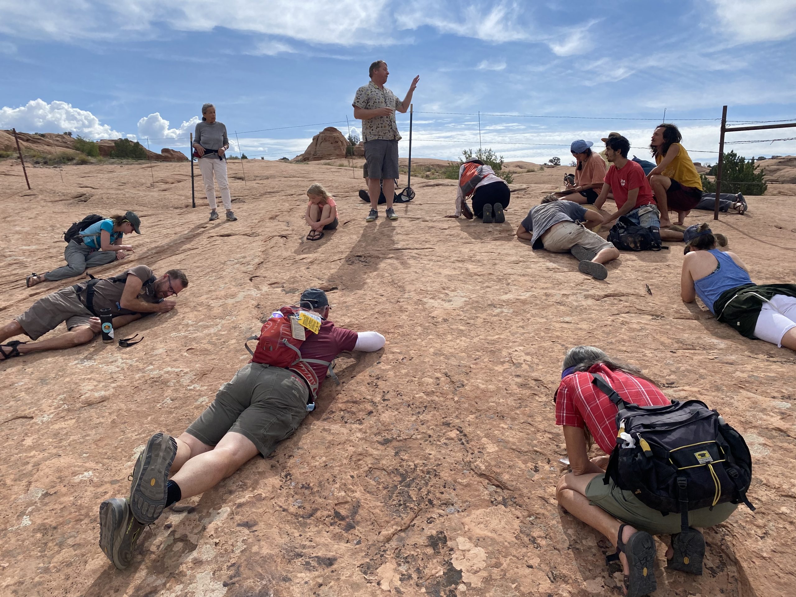 Steve Leavitt is standing in the middle of a circle of people who are all laid out on the ground, observing lichen on slickrock.