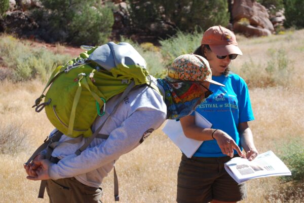 Someone in a "Festival of Science" shirt points something out in a handheld pamphlet to another person.