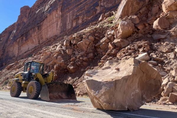 A large boulder—larger than the excavator pictured next to it—on the road.