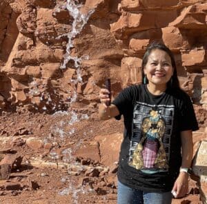 Person smiling while playing with water in front of a red rock backdrop.