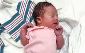 Newborn baby in pink outfit sleeps peacefully on a striped hospital blanket.