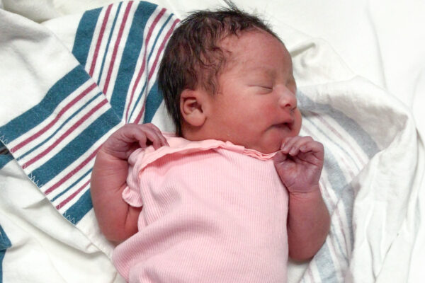 Newborn baby in pink outfit sleeps peacefully on a striped hospital blanket.
