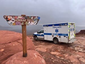 Ambulance at Hurrah Pass sign, Grand County EMS in rugged landscape with overcast skies.