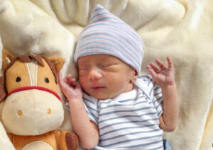 Newborn baby in striped outfit with plush toy, sleeping peacefully on soft blanket.