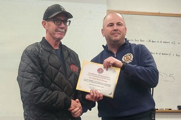 Firefighter receiving a certificate of recognition for 25 years of service in a ceremony, smiling for a photo.