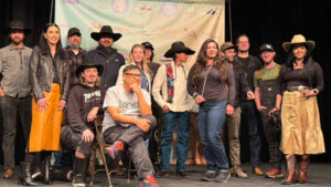 Group of diverse people in Western attire posing in front of a branded backdrop on stage.