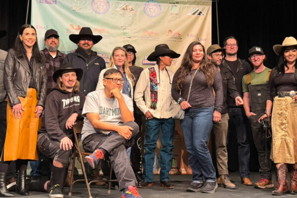 Group of diverse people in Western attire posing in front of a branded backdrop on stage.