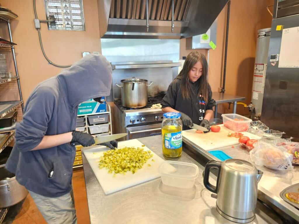 Two people carefully chopping vegetables in a commercial kitchen setting.