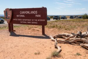 Canyonlands National Park entrance sign with parked cars in scenic desert landscape.