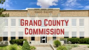Front view of Grand County Commission building under a blue sky with clouds.