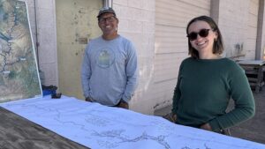 Returning Rapids Two people outdoors examining large canyon maps of the San Juan River on a wooden table.