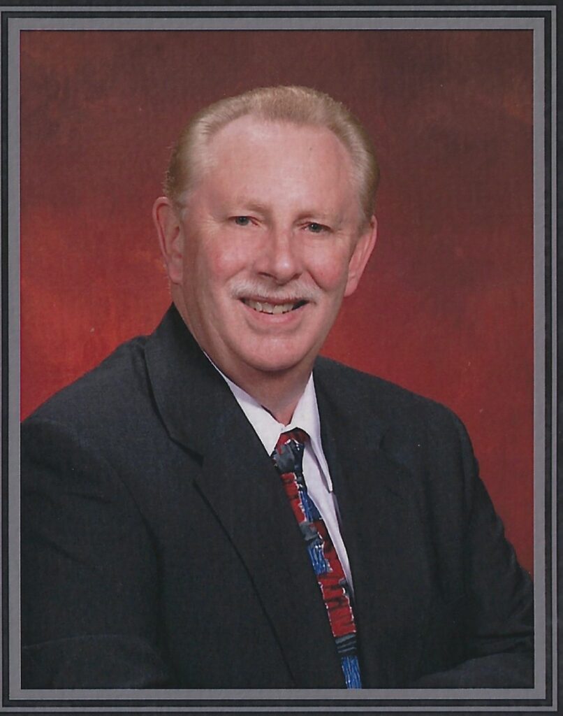 Smiling man in a suit and tie against a red background.