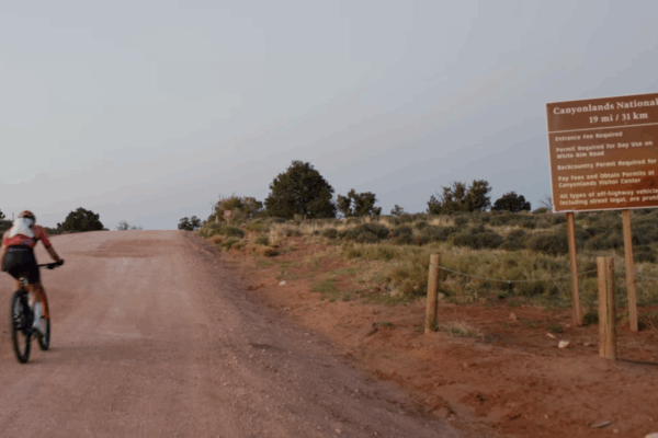 Cyclist on a trail near Canyonlands National Park sign under a clear sky.