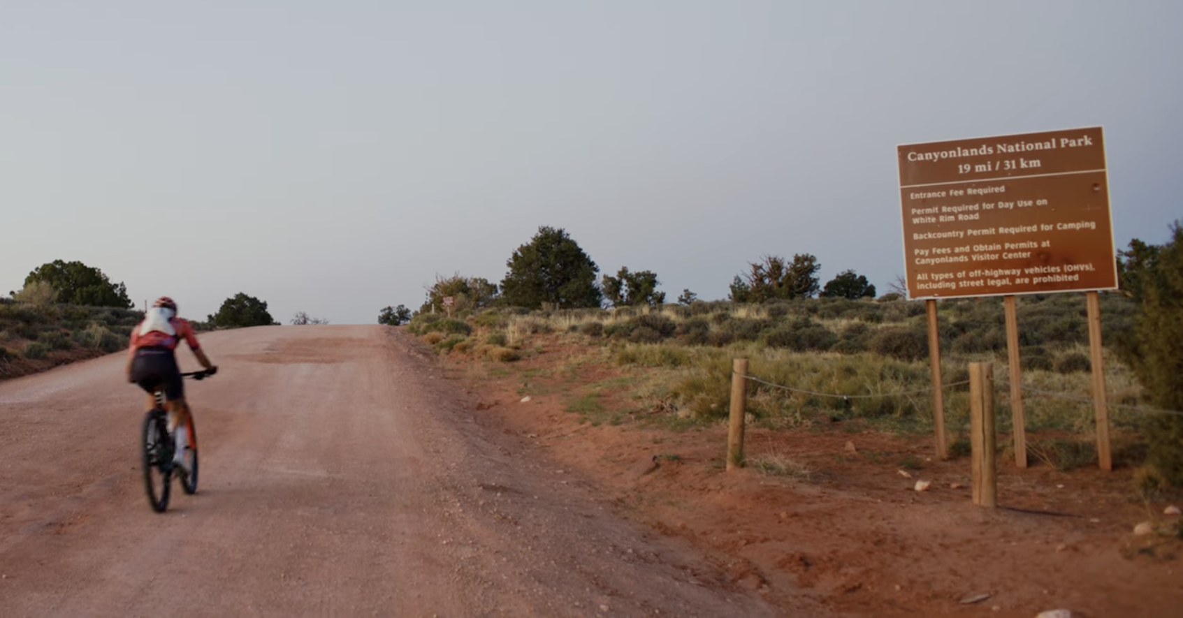 Cyclist on a trail near Canyonlands National Park sign under a clear sky.