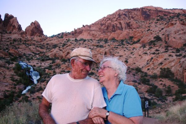 Couple smiling at desert landscape with rocky hills and waterfall in the background.