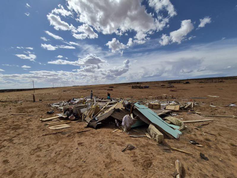 Debris scattered on arid land under a cloudy sky, indicating destruction or aftermath of an event.