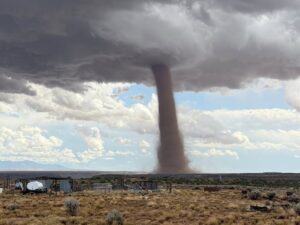 Tornado touching down in a dry, rural landscape under cloudy skies.
