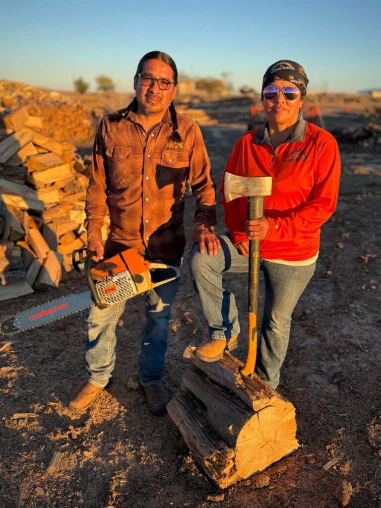 Two people with tools standing in a woodpile, representing teamwork in outdoor woodcutting activities.