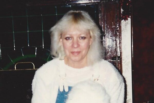 Woman kneeling with white rabbit indoors, next to a vintage fireplace. Cozy and warm setting.