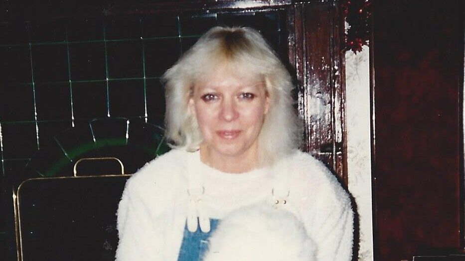 Woman kneeling with white rabbit indoors, next to a vintage fireplace. Cozy and warm setting.
