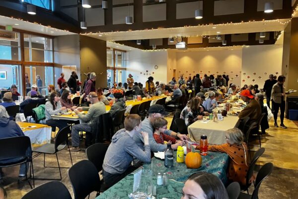 WabiSabi Thanksgiving Community gathering with people enjoying a meal at decorated tables in a festive, indoor setting.