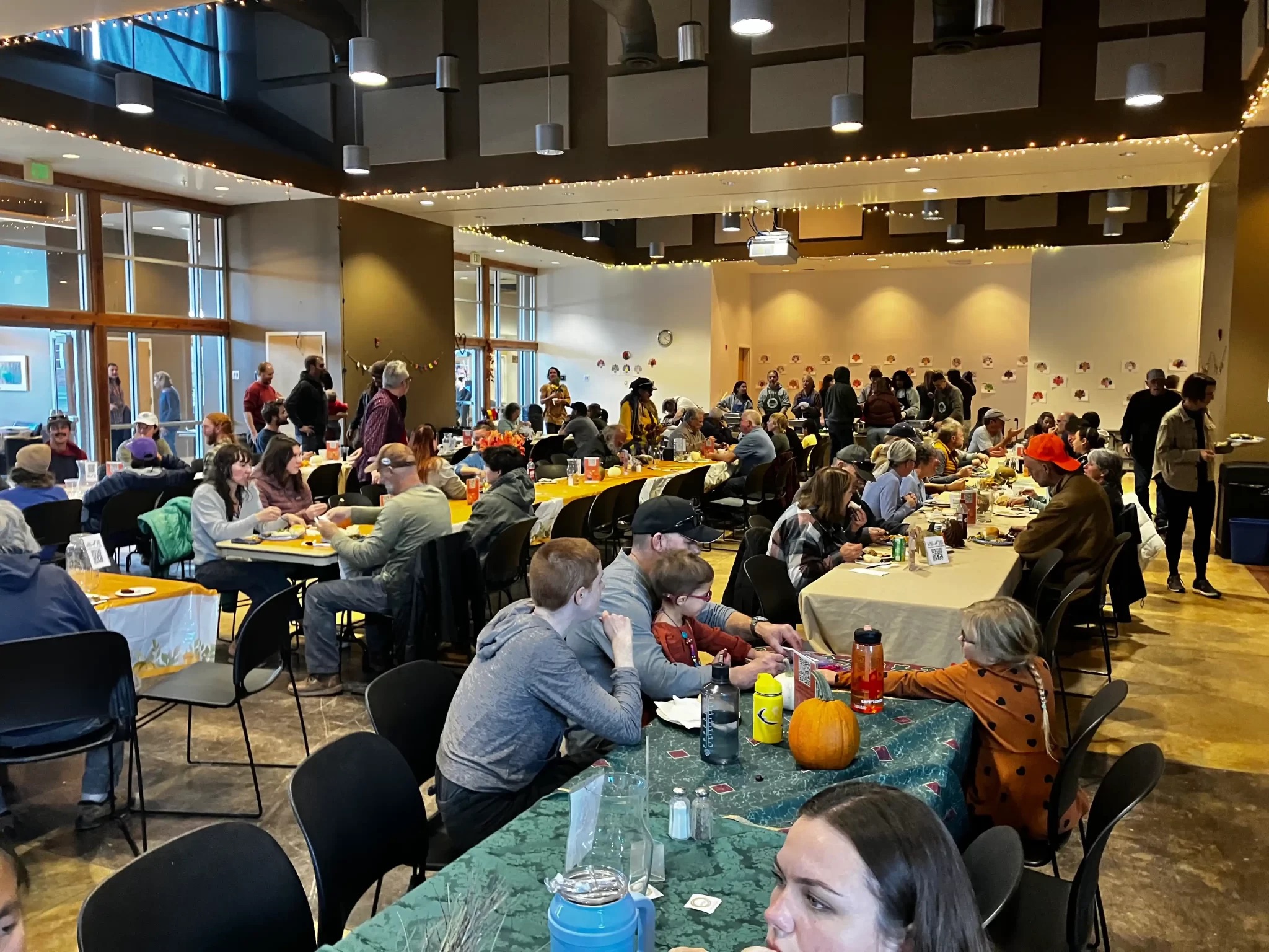 WabiSabi Thanksgiving Community gathering with people enjoying a meal at decorated tables in a festive, indoor setting.