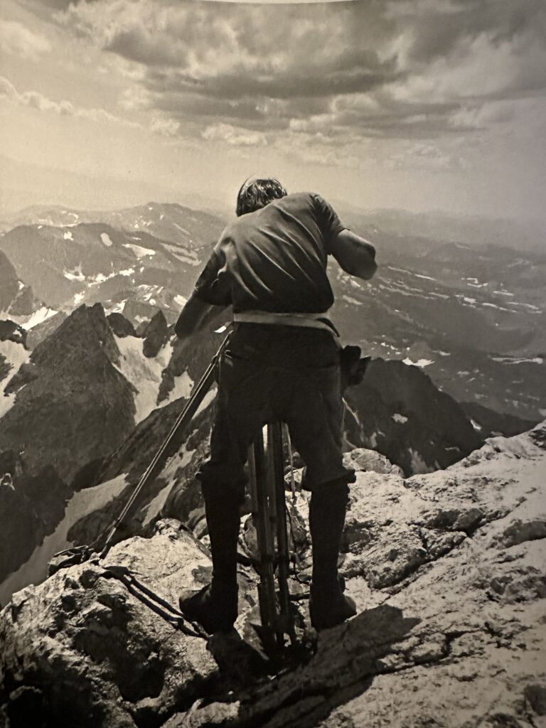 Person climbing rocky mountain with ropes under cloudy sky, showcasing adventure and mountaineering.