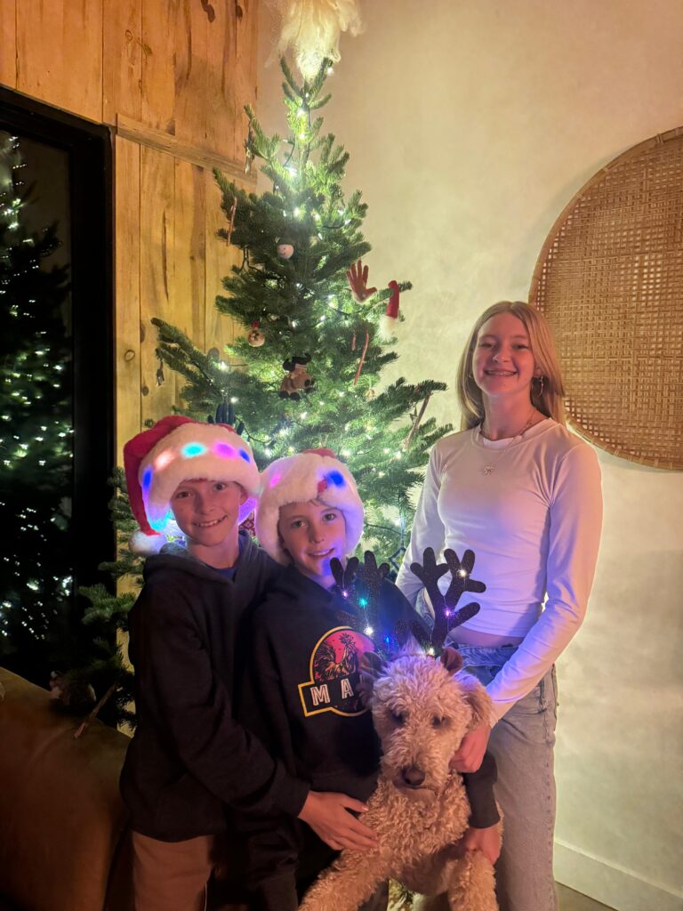 Moab's Gustafson Family celebrating Christmas with a decorated tree, wearing holiday hats, and a dog with antlers.