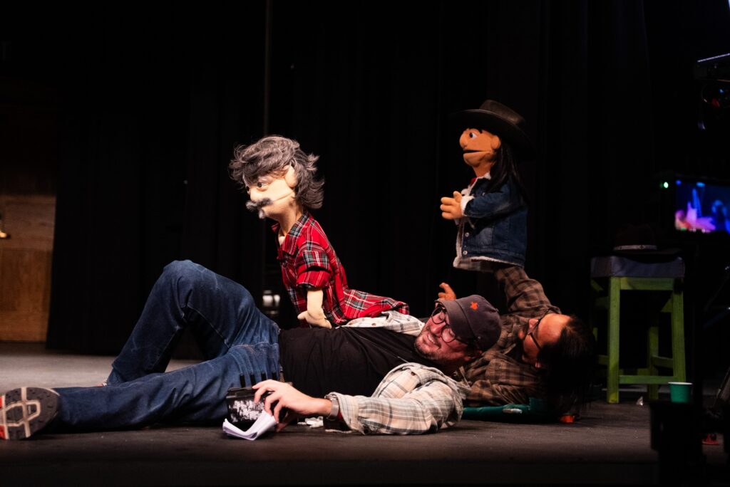 Puppeteers perform on stage with puppets in plaid and denim outfits, creating a lively and entertaining scene.