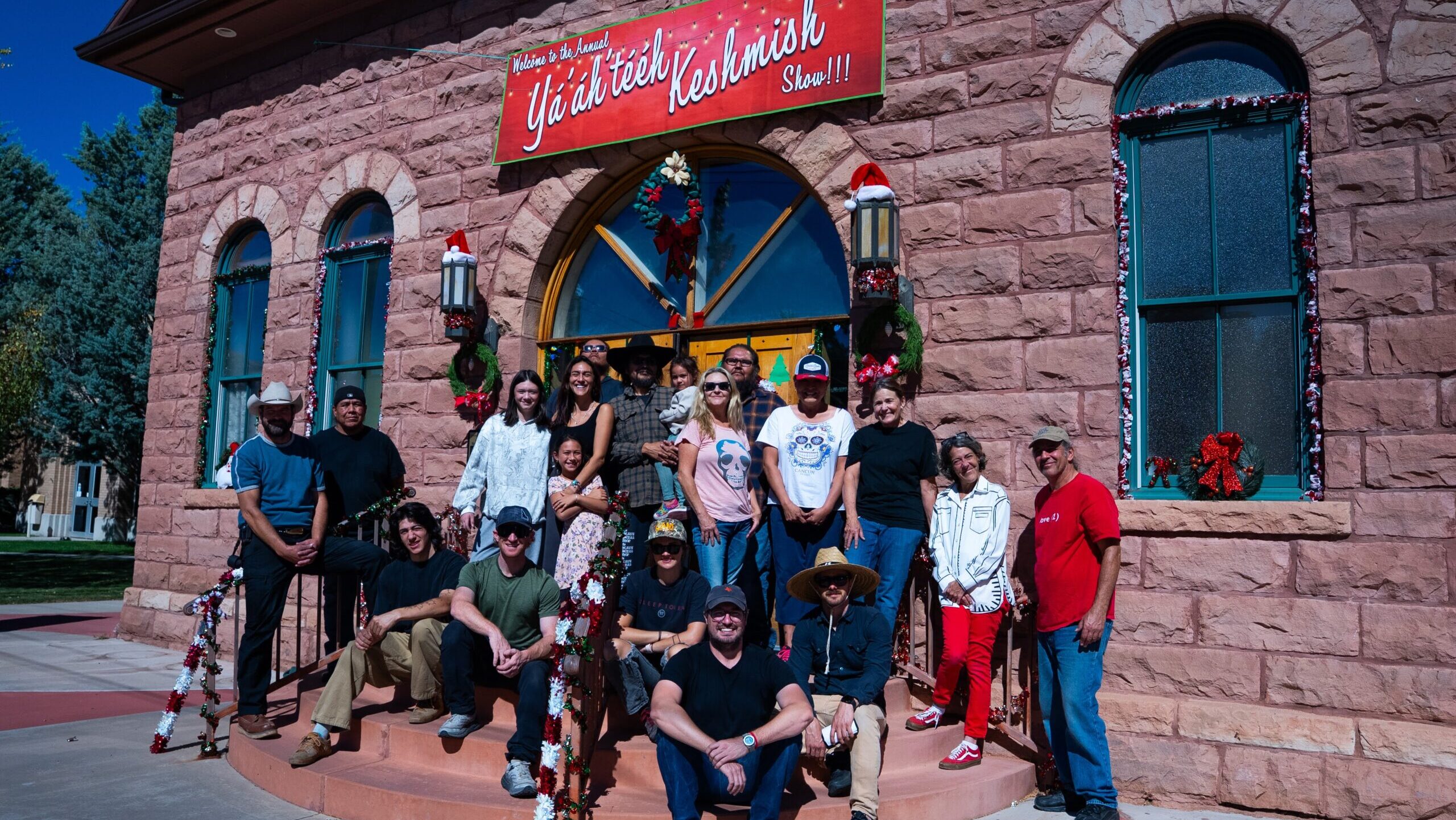 Group photo at the Yá'át'ééh Keshmish Show, people posing in front of a festive decorated building.