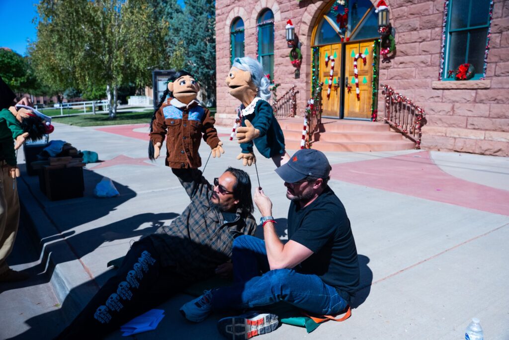 Puppeteers performing outdoors with festive decorations in the background, showcasing large puppets.